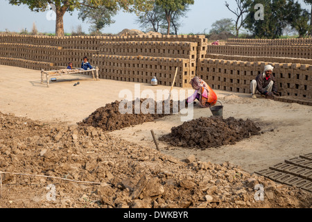 Le Rajasthan, Inde. Femme prépare de boue molle alors que mari le met dans des moules en briques tandis que deux enfants de regarder à partir d'un lit à proximité. Banque D'Images