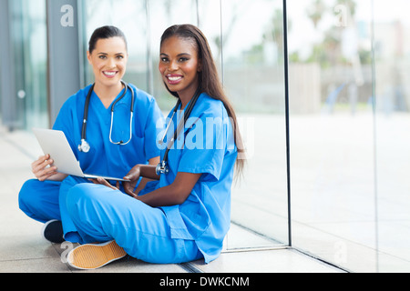 Les femmes médecins attrayant assis sur le plancher à l'aide d'ordinateur portable Banque D'Images