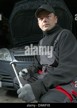 Mécanicien auto avec clé à douille posant devant une voiture avec capot surélevé Banque D'Images