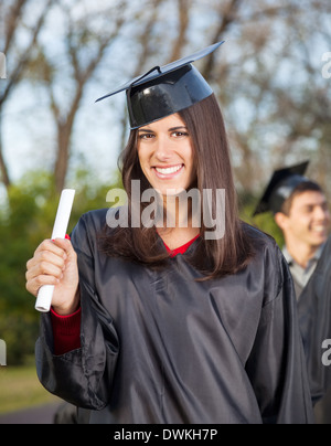Woman in Graduation Gown Holding Diploma sur College Campus Banque D'Images