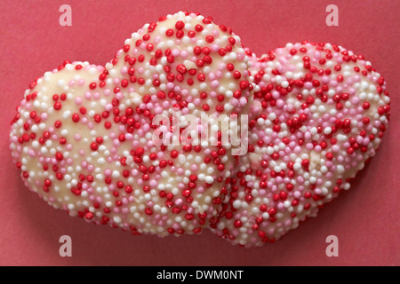 Des biscuits en forme de coeur fraises décorées avec goût vanille & revêtement rouge rose et perles de sucre blanc sur fond rouge - idéal pour la Saint-Valentin Banque D'Images