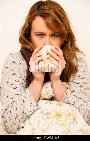 Femme malade avec feaver boire tasse de thé chaud sous couverture Banque D'Images