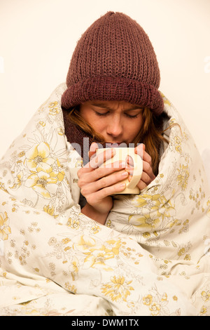 Femme malade avec feaver boire tasse de thé chaud sous couverture Banque D'Images