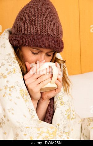 Femme malade avec feaver boire tasse de thé chaud sous couverture Banque D'Images