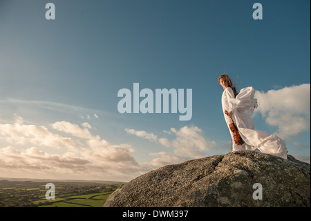 Jeune fille en blanc robe flottante avec violon debout en haut d'une colline dans le vent, Banque D'Images