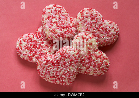 Des biscuits en forme de coeur fraises décorées avec goût vanille & revêtement rouge rose et perles de sucre blanc sur fond rouge - idéal pour la Saint-Valentin Banque D'Images