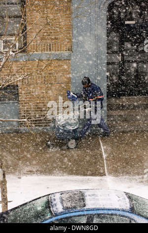 A New York City Mailman marche sur le trottoir en poussant un chariot alors que la distribution du courrier et des colis, pendant une tempête Banque D'Images