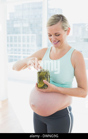Blonde pregnant woman eating de bocal de cornichons Banque D'Images