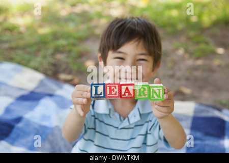 Happy boy holding alphabets bloc comme "apprendre" à park Banque D'Images