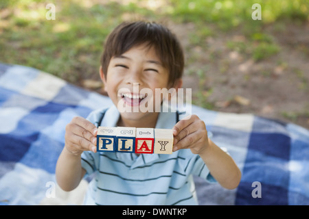 Happy boy holding alphabets bloc comme 'jouer' at park Banque D'Images