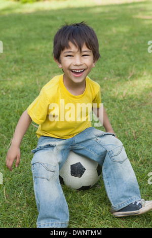 Adorable petit garçon assis sur le football at park Banque D'Images