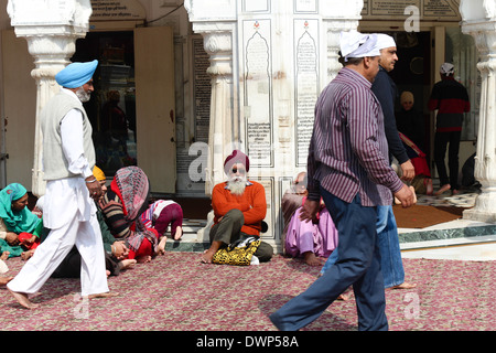 Assis à l'intérieur de dévots le Temple d'or à Amritsar, en appui sur piliers alors que d'autres sont passés à côté d'eux Banque D'Images