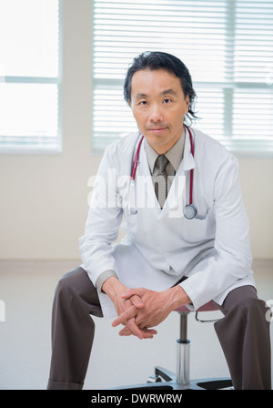 Doctor with hands clasped sitting in hospital room Banque D'Images