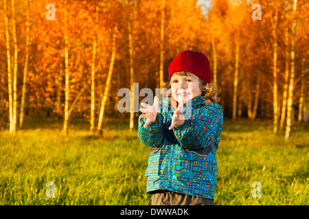 Trois ans rire petit garçon debout sur la pelouse du parc à l'automne et en tapant les mains Banque D'Images