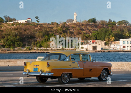 Old American Chevrolet Taxi Voiture garée sur le Malecón avec Cristo de La Habana statue dans l'arrière-plan dans Habana Vieja, Cuba Banque D'Images