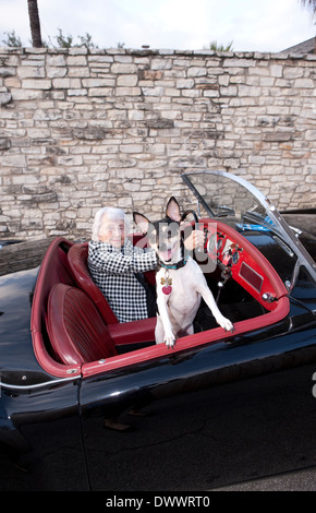 Femme âgée derrière la roue de voiture de sport avec chien dans le siège passager Banque D'Images