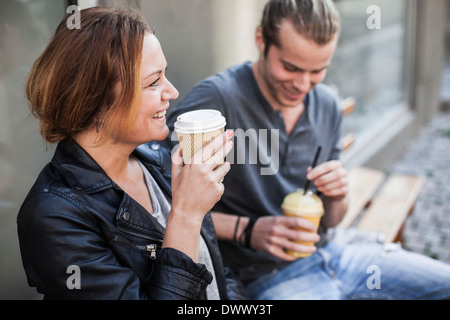 Happy woman drinking coffee in disposable cup avec l'homme sur le banc au trottoir Banque D'Images