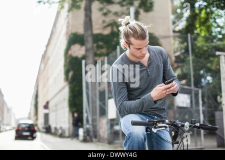 Jeune homme la messagerie texte par téléphone mobile tout en étant assis sur la rue à vélo Banque D'Images