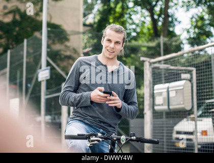 Smiling young man holding mobile phone alors que sur la rue à vélo Banque D'Images