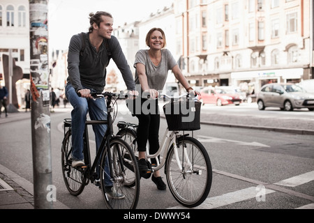 Heureux couple riding bicycles on city street Banque D'Images