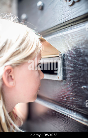 Vue latérale du girl looking through mail slot in door Banque D'Images