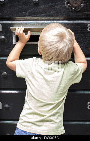 Vue arrière du petit garçon à la fente de la porte par la poste Banque D'Images