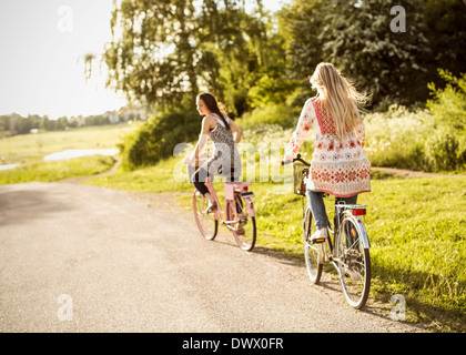 Female friends riding bicycles on country road Banque D'Images