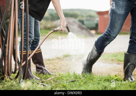 La section basse de pulvériser de l'eau femme de flexible sur la jambe de l'homme on farm Banque D'Images