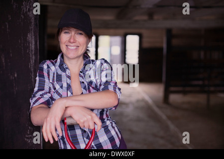 Portrait of happy female farmer et fourche debout à l'entrée de grange Banque D'Images