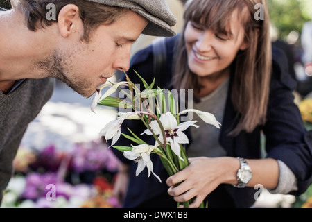 Young man smelling flowers détenues par woman in market Banque D'Images