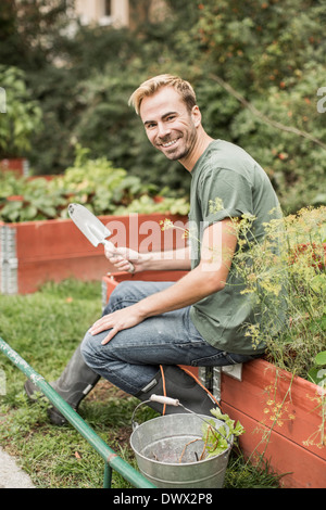 Portrait de l'homme heureux avec équipement de jardinage assis dans le jardin Banque D'Images