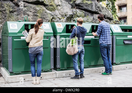 Vue arrière d'amis mettre matières recyclables dans les bacs de recyclage Banque D'Images