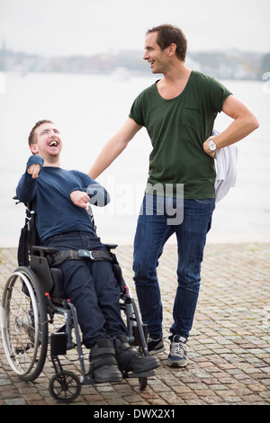 Homme debout avec gardien heureux homme handicapé sur fauteuil roulant par lake Banque D'Images