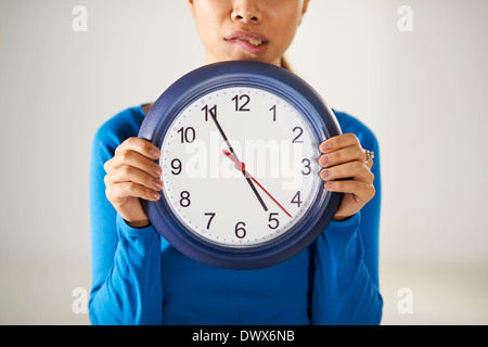 Portrait of asian business woman holding big blue watch and looking at camera avec expression inquiète Banque D'Images