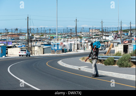 Homme portant un sac traverse une route à Khayelitsha, Cape Town, Western Cape, Afrique du Sud Banque D'Images