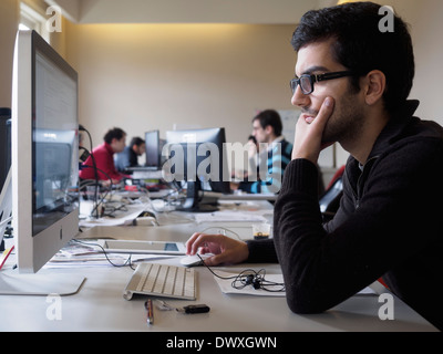 Un homme à l'aide d'un ordinateur Apple iMac dans un bureau open space Banque D'Images