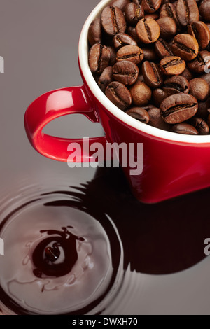 Les grains de café naturel sur un mug rouge sur fond reflétée. Banque D'Images