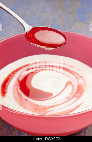 Cuillère pleine de confiture de fraise prêt à mélanger avec du yaourt pot. Banque D'Images