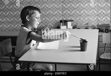 Berlin, RDA, un petit garçon assis à une table et brosse un tableau à l'aquarelle Banque D'Images