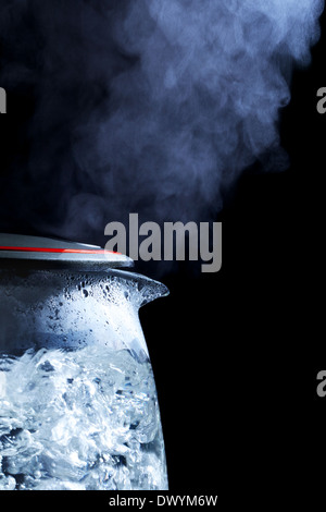 Bouilloire électrique en verre avec de l'eau bouillante, fond noir Banque D'Images