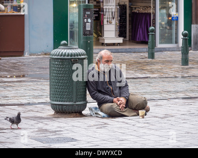 Un sans-abri assis sur une rue humide à Bruxelles, Belgique. Banque D'Images