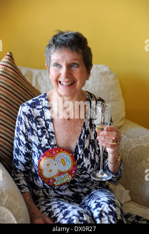 Femme âgée qui célèbre son 80e anniversaire avec un verre de champagne Banque D'Images