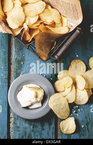 Vue de dessus sur panier avec les chips de pomme de terre avec la plaque de sause et de sel de mer sur table en bois bleu. Banque D'Images