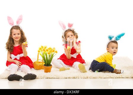 Trois enfants avec des oreilles de lapin et panier de Pâques assis sur le tapis home Banque D'Images