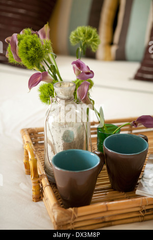 Fleurs dans un vase et tasses sur plateau en bambou sur lit, Close up, high angle view Banque D'Images