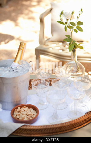 Bouteille de champagne au frais dans un seau à glace en argent sur le bac avec des verres de champagne et les amandes marcona sur patio ensoleillé, high angle vie Banque D'Images