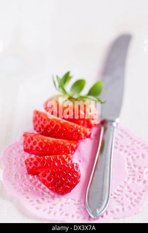 Libre de fraises fraîches, tranchées avec couteau en métal argenté reposant sur le tapis rose décorative Banque D'Images