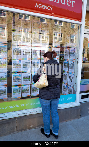 Une femme d'âge moyen à la recherche dans une fenêtre d'agents immobiliers Bakewell Derbyshire, Angleterre, Royaume-Uni Banque D'Images