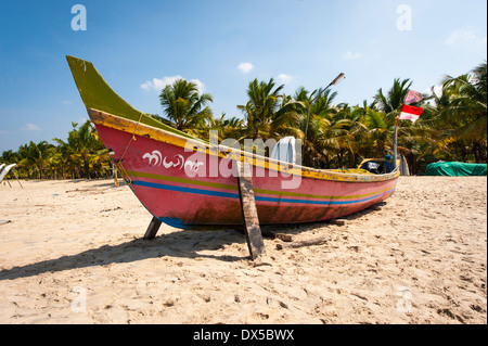 Le Sud de l'Inde du Sud Kerala Alleppy Mararikulam bateau de pêche de la plage de sable de la rive en bois soleil ciel bleu, décor de scène enseignes drapeaux Banque D'Images