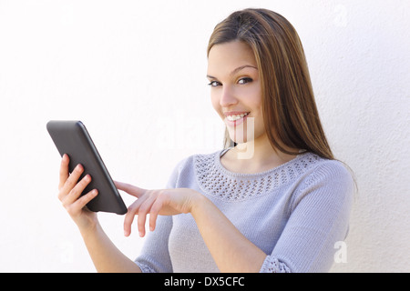 Beautiful woman smiling and holding a tablet reader et looking at camera sur un mur blanc Banque D'Images